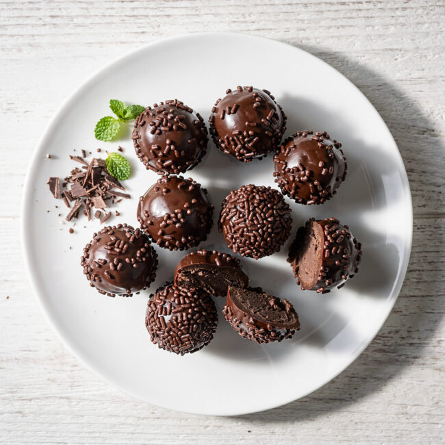 A beautifully styled overhead shot of the finished brigadeiro recipe, featuring glossy chocolate truffles rolled in colorful sprinkles.