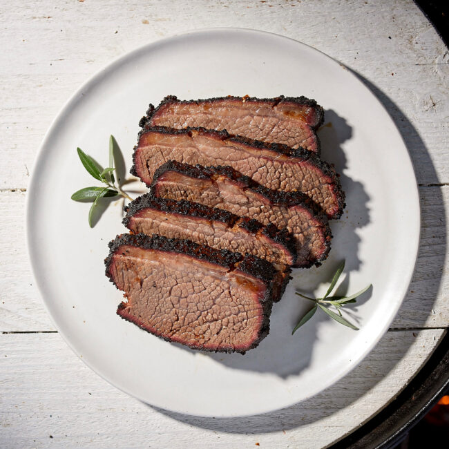 A perfectly smoked brisket on the grill, showcasing a dark, crackly bark and juicy pink interior, sliced and ready to serve.