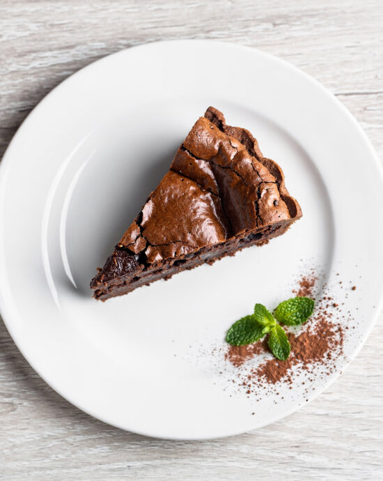 A slice of rich brownie pie with a flaky crust sits on a plate, showing its fudgy interior.