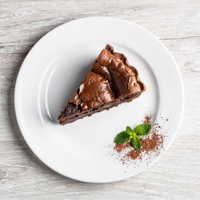 A slice of rich brownie pie with a flaky crust sits on a plate, showing its fudgy interior.