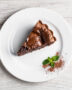 A slice of rich brownie pie with a flaky crust sits on a plate, showing its fudgy interior.