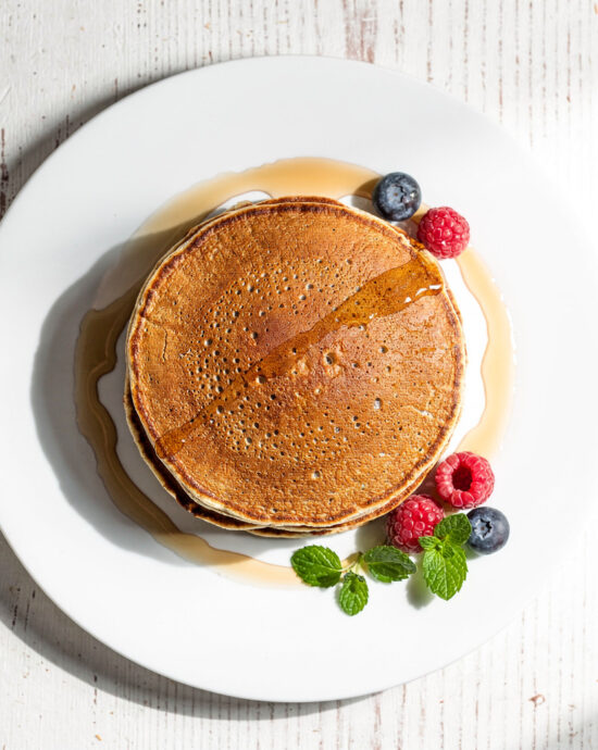 A stack of fluffy, speckled brown buckwheat pancakes drizzled with maple syrup.