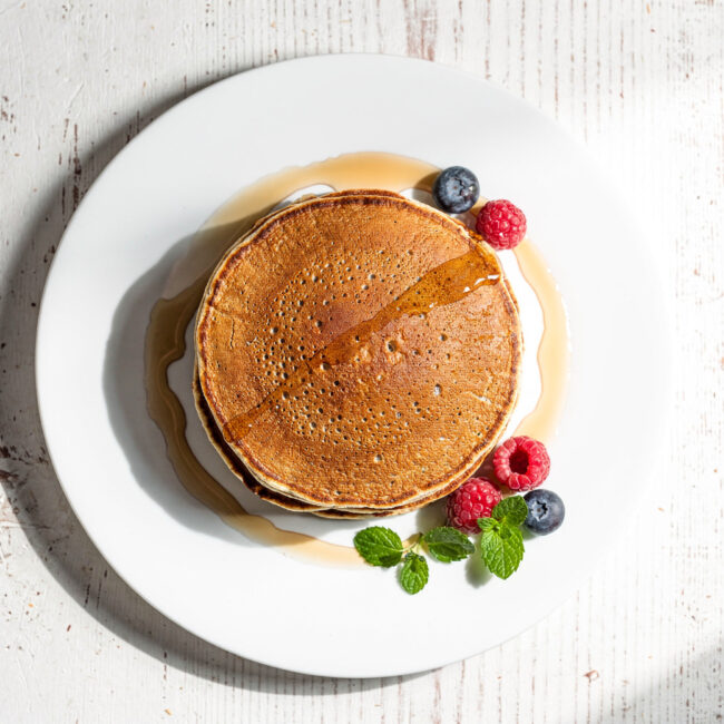 A stack of fluffy, speckled brown buckwheat pancakes drizzled with maple syrup.