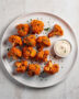 A golden-brown batch of crispy buffalo cauliflower served with creamy dip and celery sticks on a rustic wooden board.
