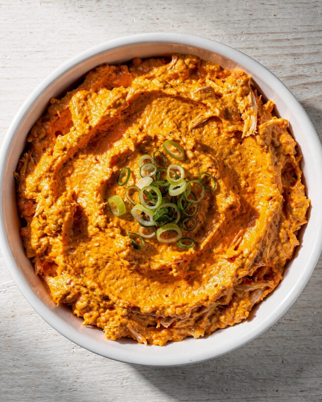A bubbling, golden-brown buffalo dip in a rustic white ceramic dish, ready for dipping.