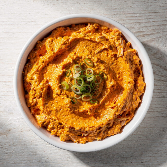 A bubbling, golden-brown buffalo dip in a rustic white ceramic dish, ready for dipping.