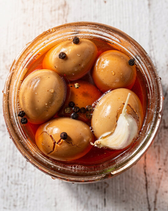 A rustic jar filled with vibrant buffalo pickled eggs, sitting on a wooden table.