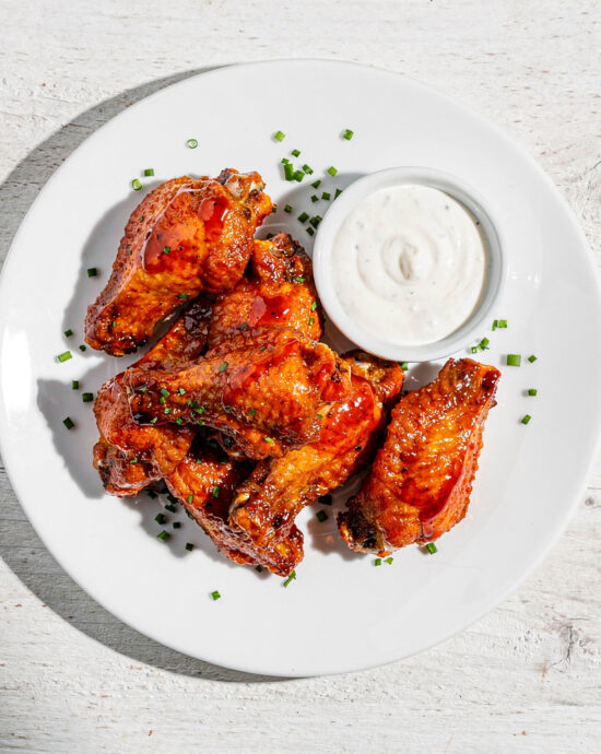 A platter of crispy buffalo wings and dip, ready for sharing on a rustic wooden table.