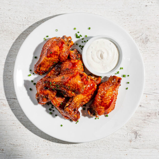 A platter of crispy buffalo wings and dip, ready for sharing on a rustic wooden table.
