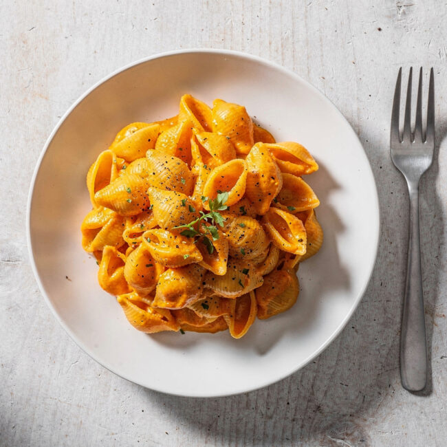 A creamy, golden serving of butternut squash mac and cheese in a white bowl on a rustic table.