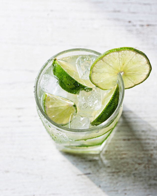 A classic caipirinha cocktail in a heavy rocks glass, with muddled lime and crushed ice, sitting on a rustic wooden table.