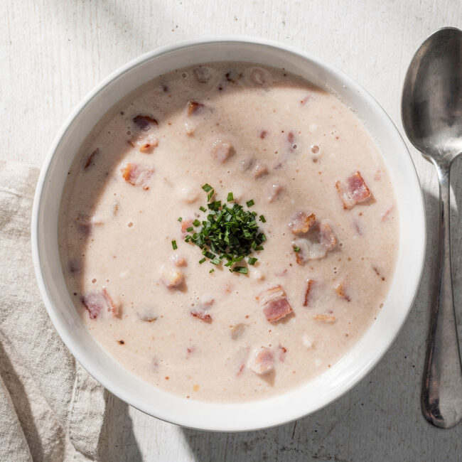 A bowl of homemade Campbell's cream of bacon soup with crispy bacon bits on top, served on a wooden table.