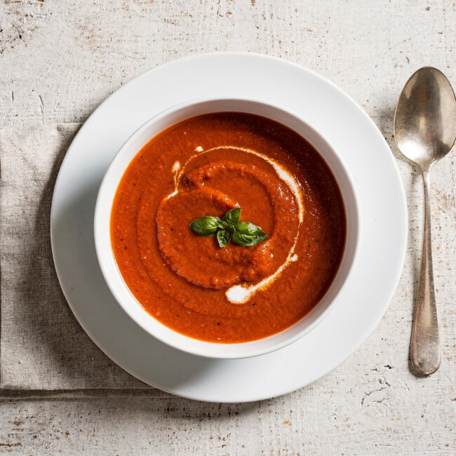 A beautifully styled bowl of homemade campbell's tomato basil soup on a rustic wooden table.