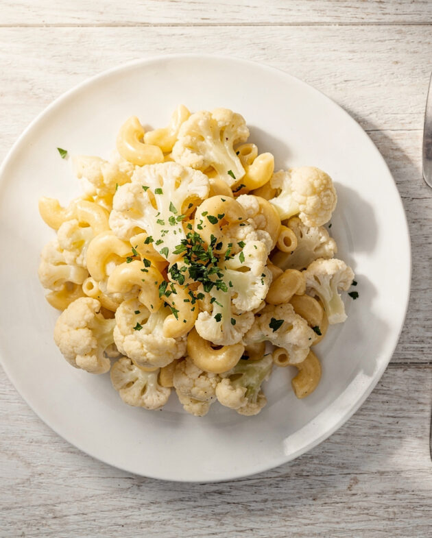 A creamy, golden-brown cauliflower mac and cheese casserole with a bubbly cheese crust, served in a white baking dish.