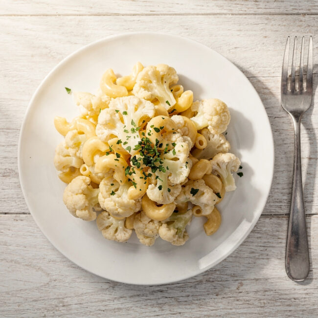 A creamy, golden-brown cauliflower mac and cheese casserole with a bubbly cheese crust, served in a white baking dish.