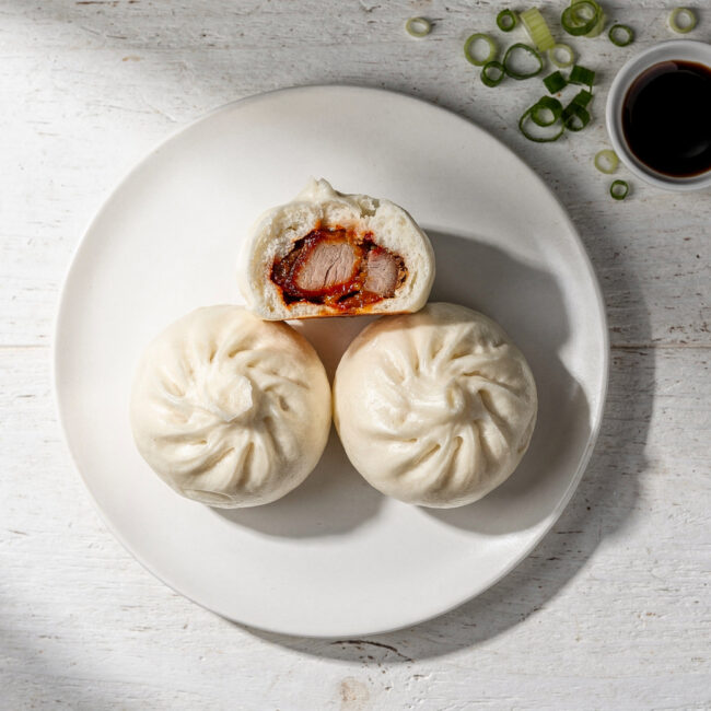 A bamboo steamer overflowing with freshly steamed char siu bao, glistening under soft light.