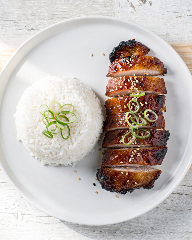 A close-up shot of glossy, caramelized char siu chicken thighs, served on a bed of fluffy white rice.