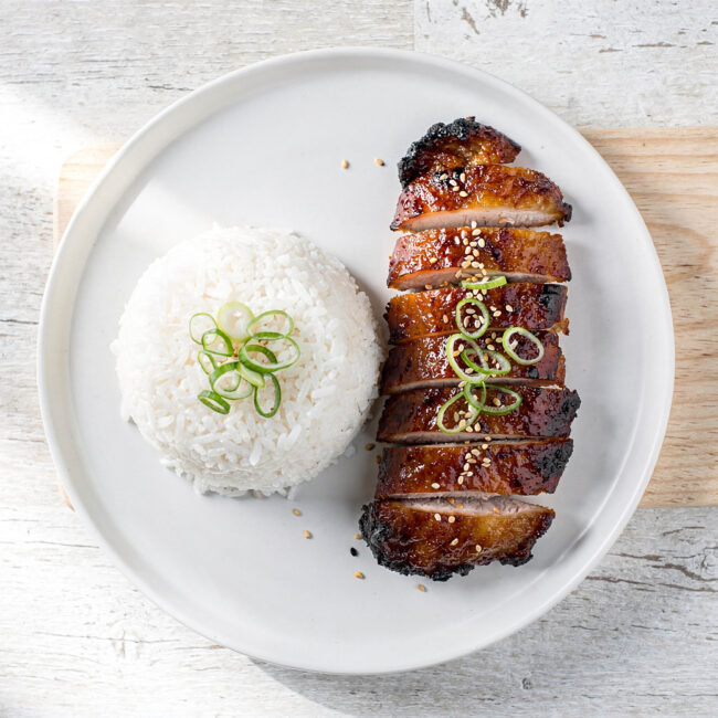 A close-up shot of glossy, caramelized char siu chicken thighs, served on a bed of fluffy white rice.