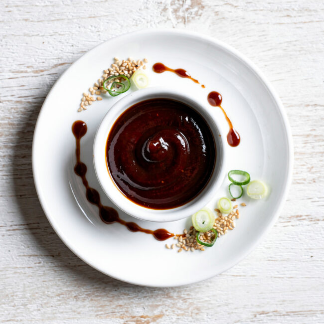 A glossy, deep red char siu sauce drizzled over succulent roast pork in a bowl.