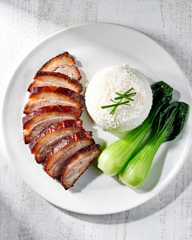 A close-up shot of glossy, freshly sliced char siu pork resting on a wooden cutting board.