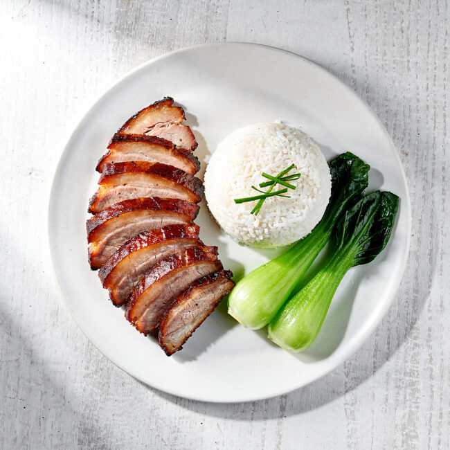 A close-up shot of glossy, freshly sliced char siu pork resting on a wooden cutting board.