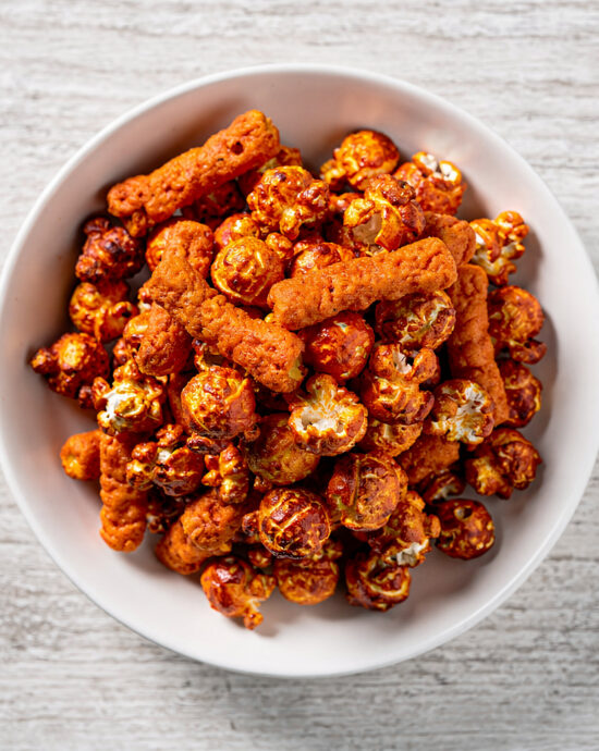 A close-up of a bowl of delicious cheetos flamin hot popcorn, coated in a vibrant orange cheese seasoning.