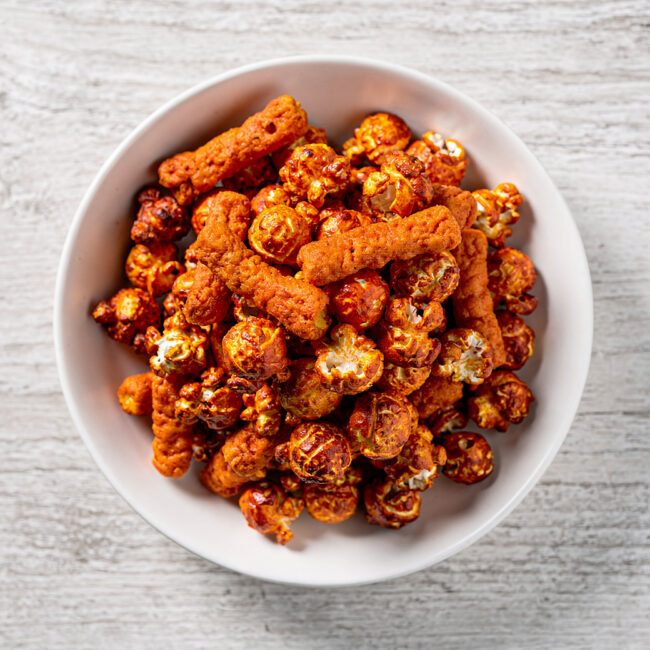 A close-up of a bowl of delicious cheetos flamin hot popcorn, coated in a vibrant orange cheese seasoning.