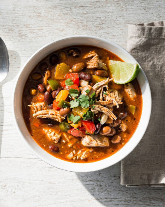 A vibrant bowl of this easy chicken chili recipe, topped with avocado and cilantro, sits on a rustic wooden table.