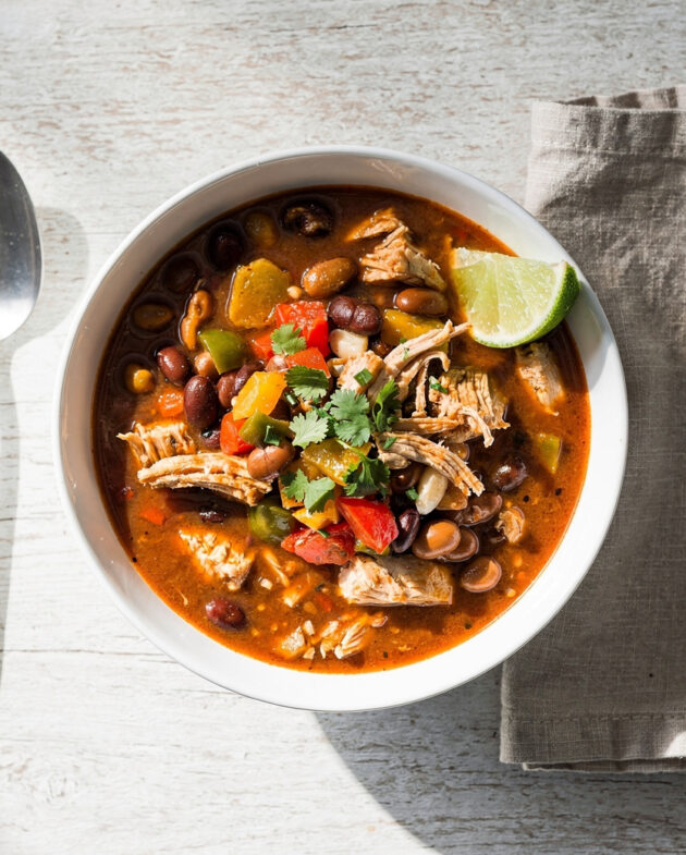 A vibrant bowl of this easy chicken chili recipe, topped with avocado and cilantro, sits on a rustic wooden table.