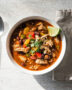 A vibrant bowl of this easy chicken chili recipe, topped with avocado and cilantro, sits on a rustic wooden table.