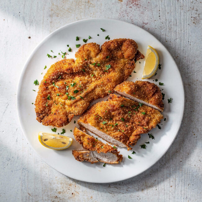 Crispy, golden-brown chicken cutlets plated elegantly on a wooden board with lemon wedges.