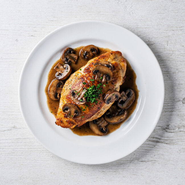 A glossy, perfectly cooked chicken marsala served over creamy polenta, garnished with fresh parsley.