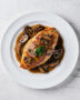 A glossy, perfectly cooked chicken marsala served over creamy polenta, garnished with fresh parsley.
