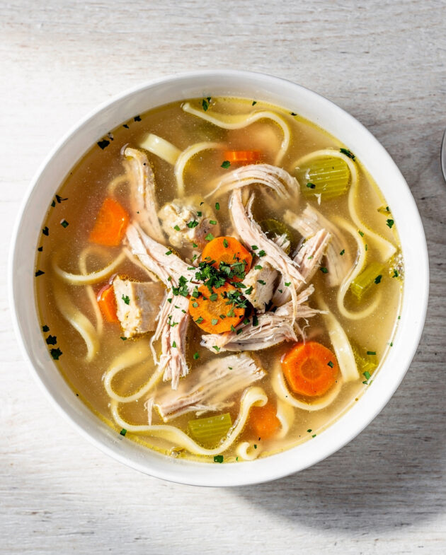 A steaming bowl of our classic chicken noodle soup recipe sits on a rustic wooden table.