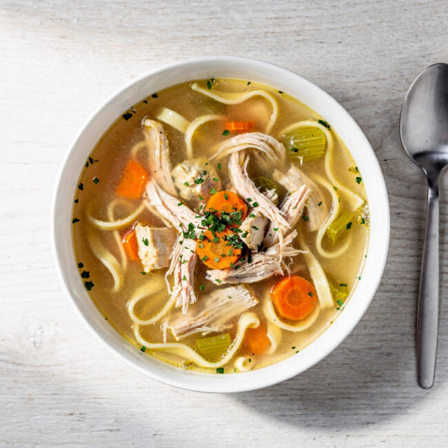A steaming bowl of our classic chicken noodle soup recipe sits on a rustic wooden table.