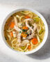 A steaming bowl of our classic chicken noodle soup recipe sits on a rustic wooden table.
