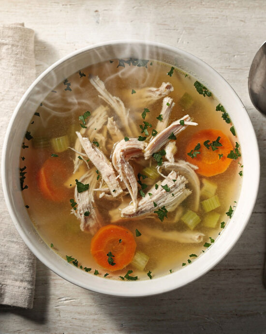 A steaming bowl of homemade chicken soup with carrots, celery, and tender chicken, garnished with fresh dill.