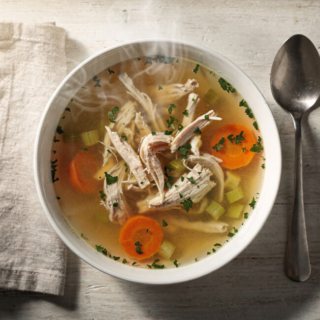 A steaming bowl of homemade chicken soup with carrots, celery, and tender chicken, garnished with fresh dill.
