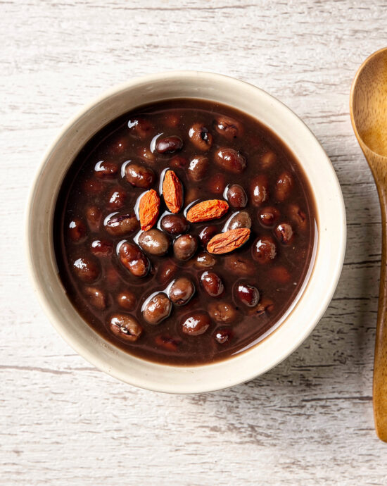 A comforting bowl of traditional chinese desserts, specifically red bean soup, gently steaming and garnished with red goji berries.