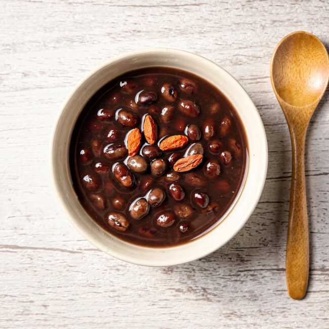 A comforting bowl of traditional chinese desserts, specifically red bean soup, gently steaming and garnished with red goji berries.