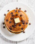 A tall stack of golden chocolate chip pancakes drizzled with syrup, ready for a cozy breakfast.