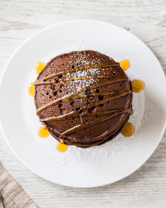 A tall, fluffy stack of perfect chocolate pancakes drizzled with maple syrup, ready for a decadent breakfast.