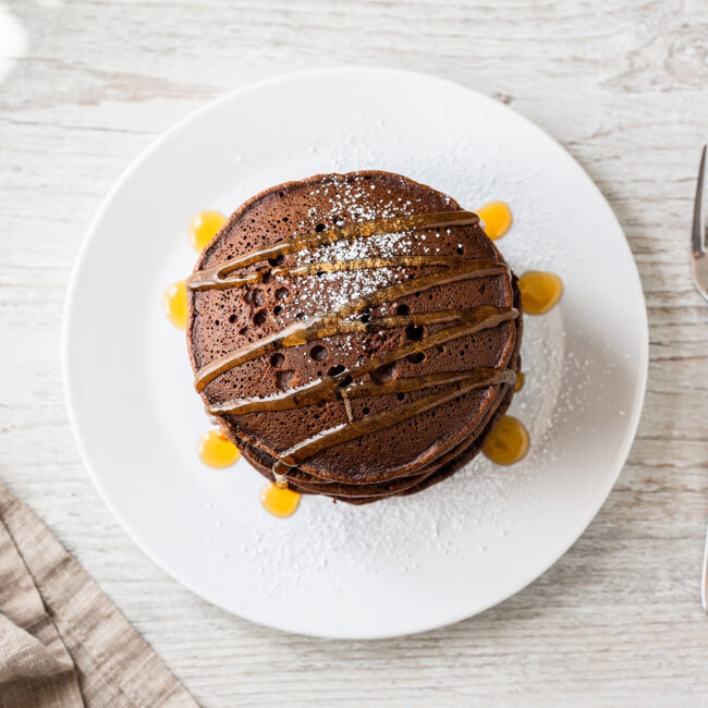 A tall, fluffy stack of perfect chocolate pancakes drizzled with maple syrup, ready for a decadent breakfast.