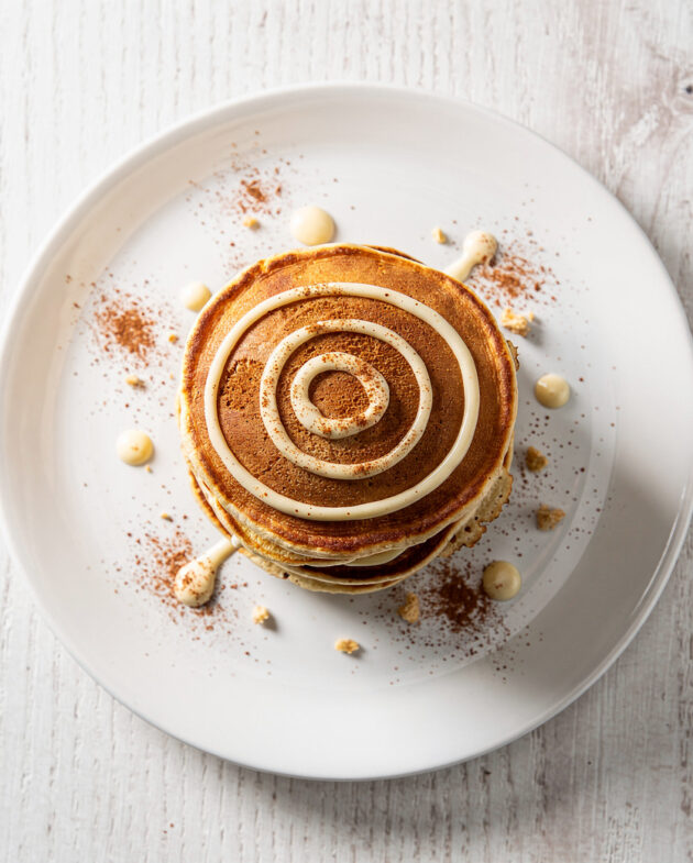A stack of fluffy cinnamon roll pancakes drizzled with cream cheese glaze, ready for a cozy breakfast.