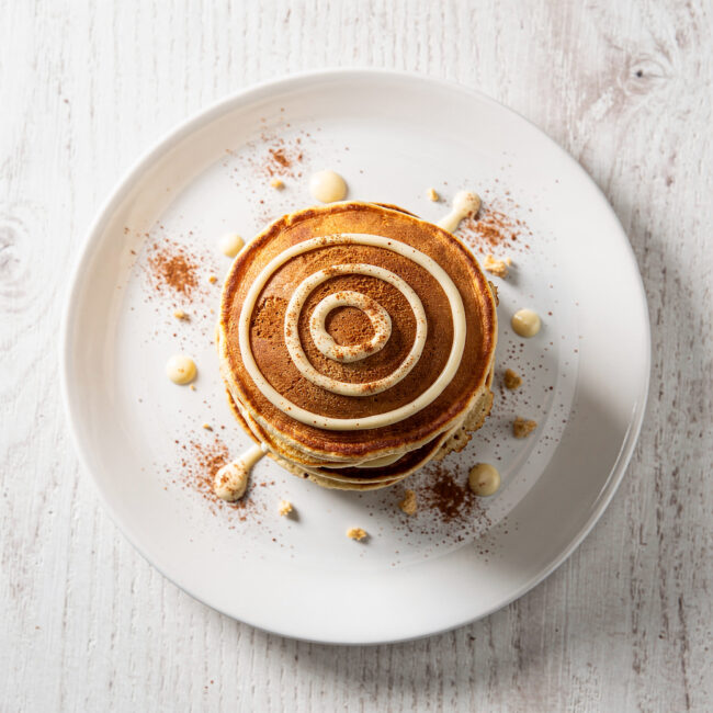 A stack of fluffy cinnamon roll pancakes drizzled with cream cheese glaze, ready for a cozy breakfast.