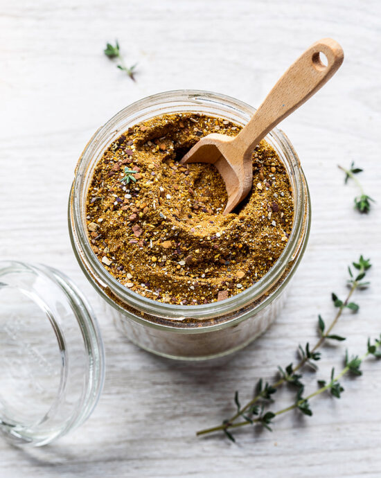 A jar of homemade condensed french onion soup mix sits on a rustic wooden table with a spoon.