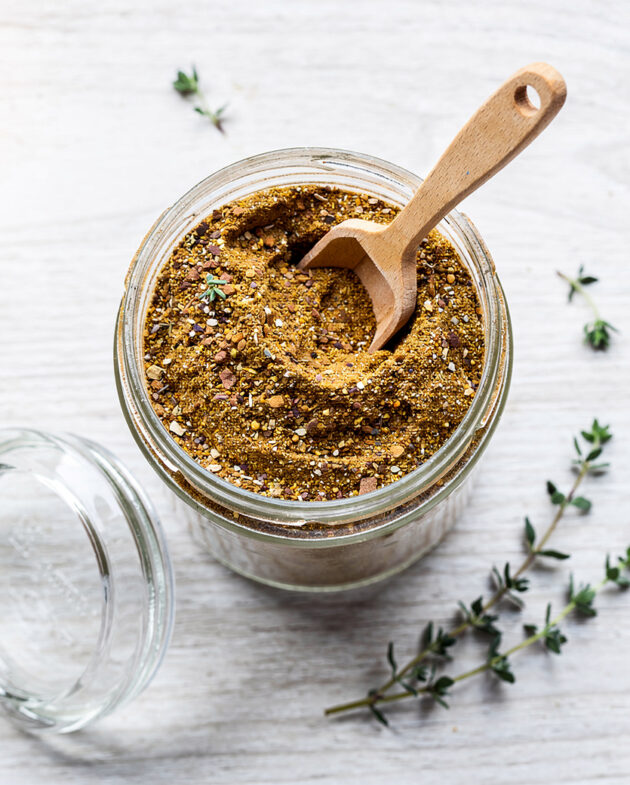 A jar of homemade condensed french onion soup mix sits on a rustic wooden table with a spoon.
