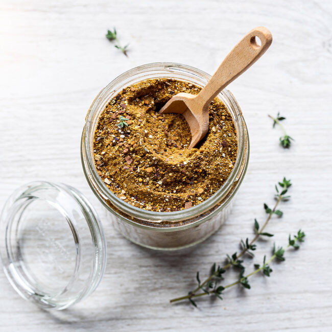 A jar of homemade condensed french onion soup mix sits on a rustic wooden table with a spoon.