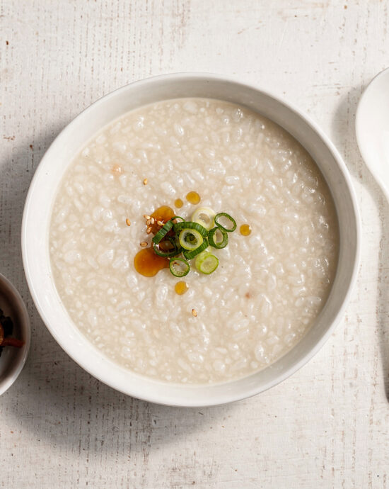 A beautifully styled bowl of creamy congee rice porridge garnished with green onion and a drizzle of sesame oil.