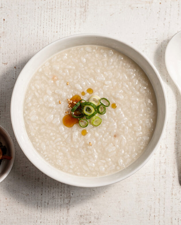 A beautifully styled bowl of creamy congee rice porridge garnished with green onion and a drizzle of sesame oil.
